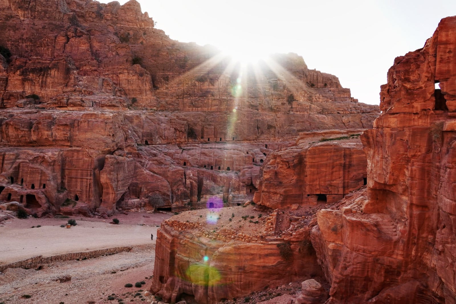 Die Sonne verschwindet hinter den Bergen, im Vordergrund die Felsenstadt Petra in Jordanien.